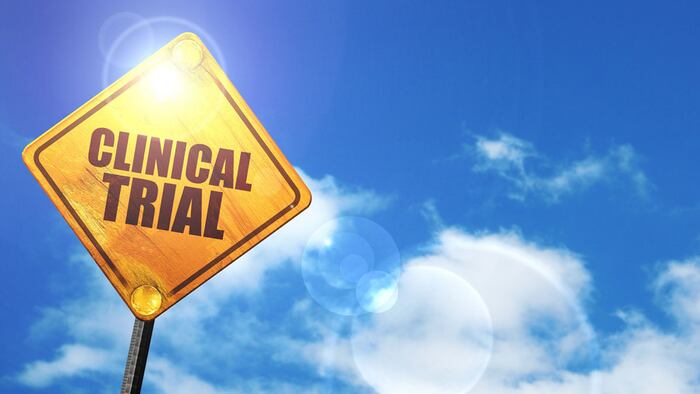 Yellow road sign with a blue sky and white clouds: clinical trial