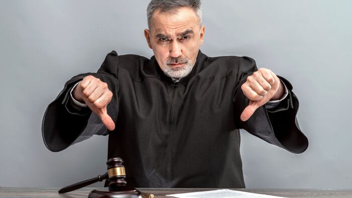 Older man with beard in judge's robe giving thumbs down.