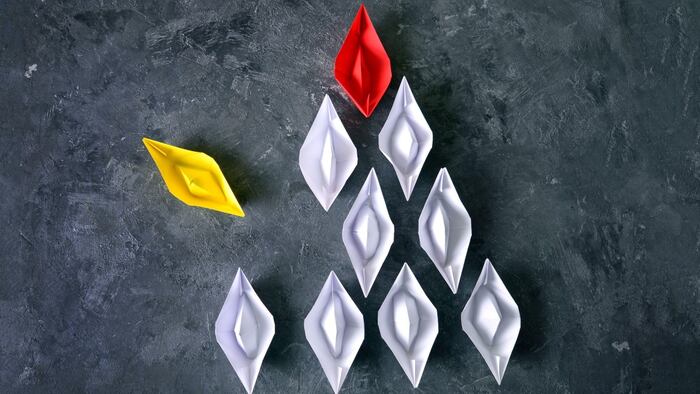 Yellow paper boat breaks out of order from other paper boats