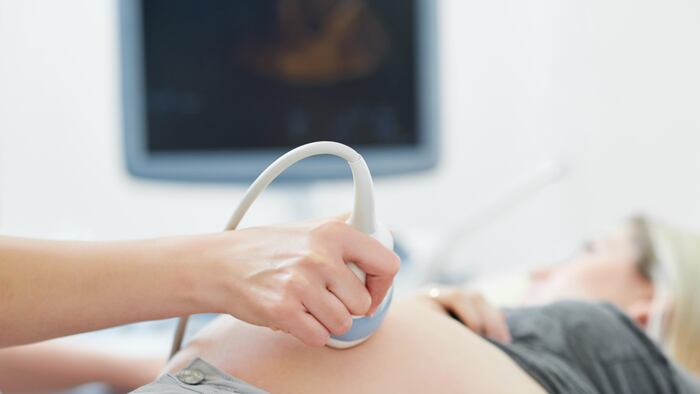 Crop of hand of professional doctor using ultrasound equipment and gel screening of pregnant woman. Doctor touching stomach by tool of female who lying and looking at screen of computer