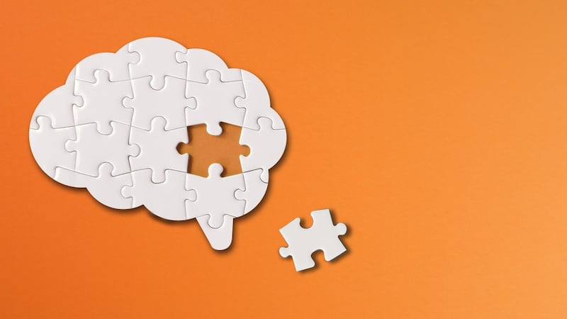 White jigsaw puzzle of the brain with one missing piece out on the side, orange background