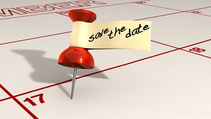 A calendar with an attached red thumbtack with a tape tag and the words save the date written in black marker