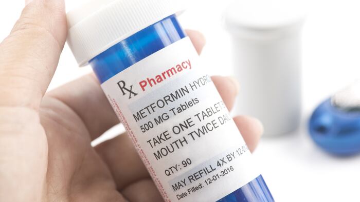 Close up of Metformin prescription bottle with glucometer and testing strip container.