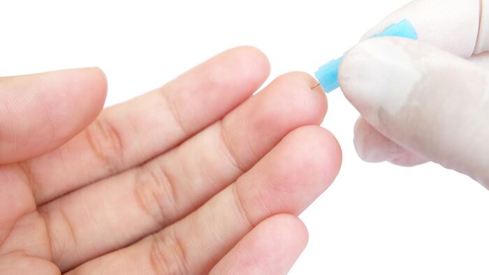 blue blood lancet penetrates to the skin of left hand with white background (isolated and have clipping path)