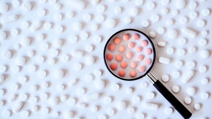 Concept of health care, medicine, pharmacy, COVID-19, coronavirus. Assortment of pharmaceutical products, white and pink pills with a magnifying glass